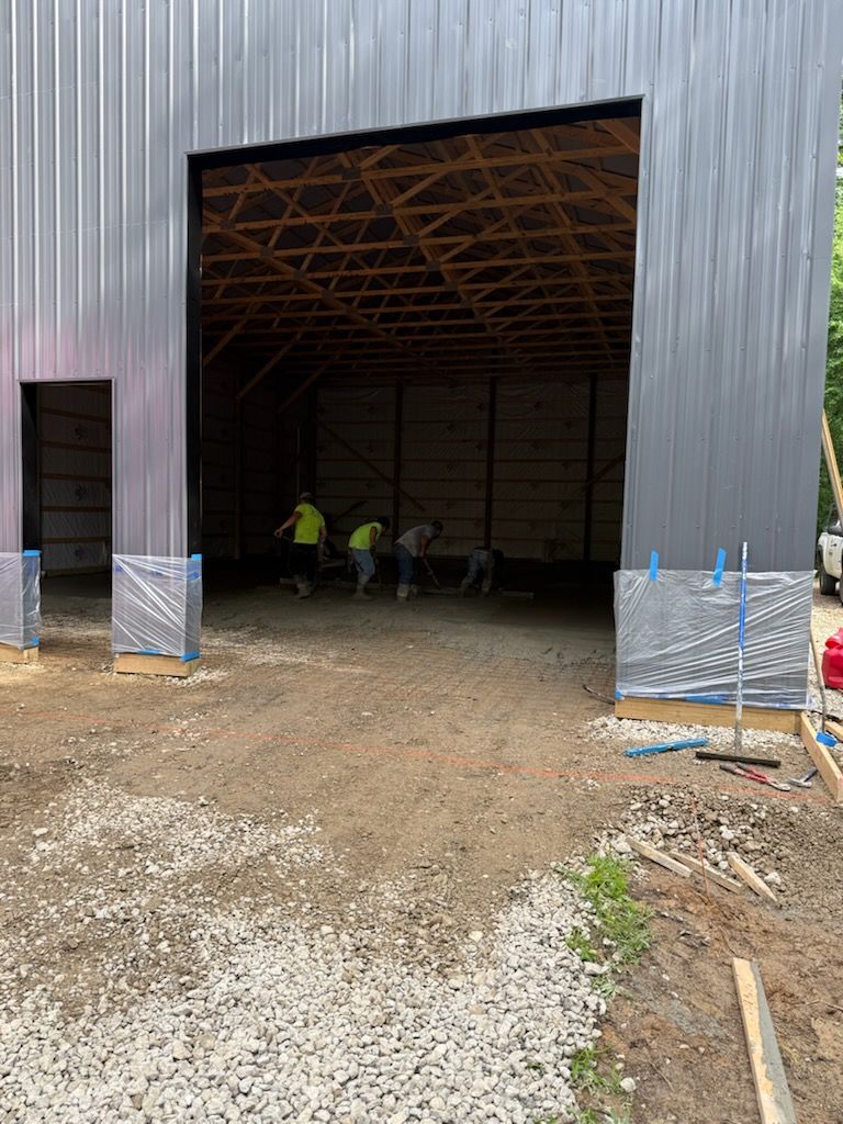 Construction workers inside a large metal warehouse doorway, with gravel and equipment outside.