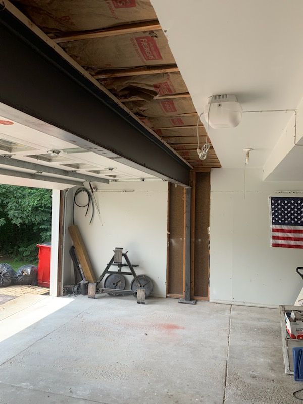 An interior view of a garage showing an exposed ceiling, a large metal support beam, and a wall-mounted American flag.