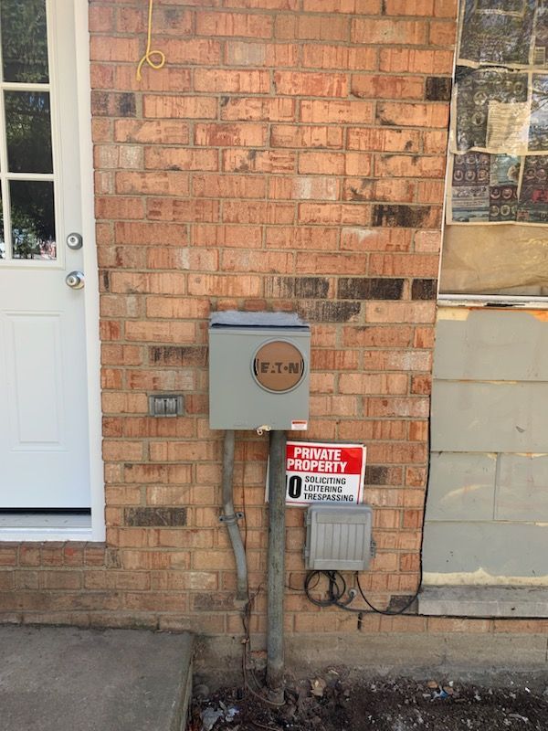 An electrical meter box on a red brick exterior wall next to a white door, with a private property sign below.