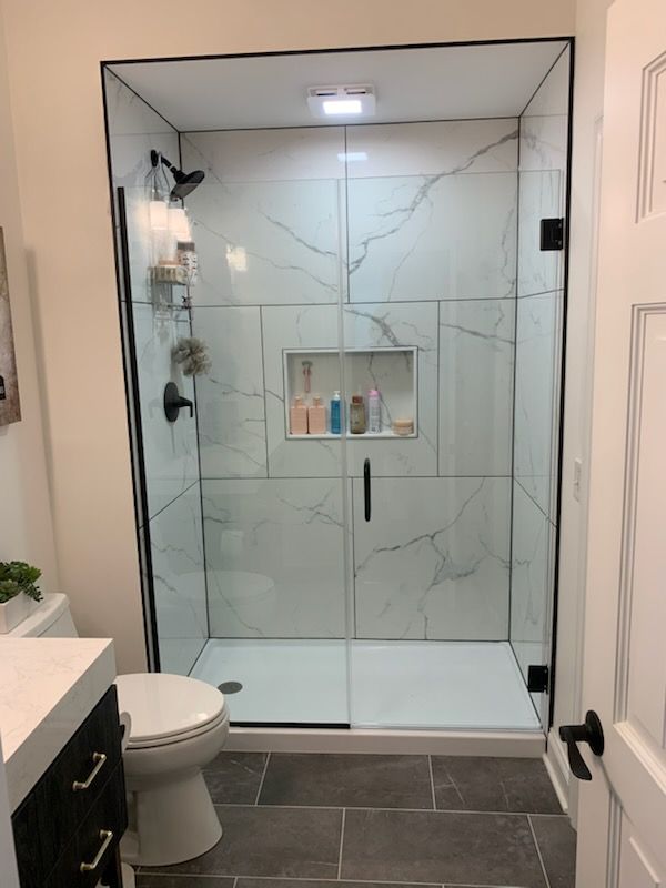 A walk-in shower with white marble-patterned tile, a glass door, and black fixtures in a modern bathroom with tile floors.