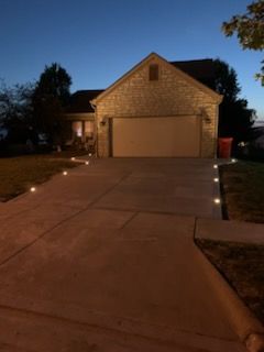 A suburban house exterior at dusk with small solar lights illuminating the driveway edges leading to the garage.