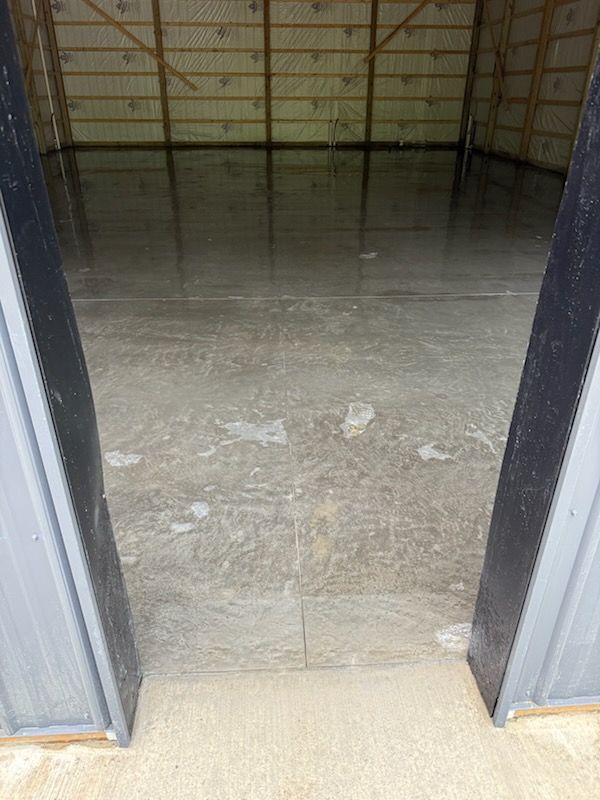 Open doorway to a bare concrete interior with a metal-framed wall and floor.