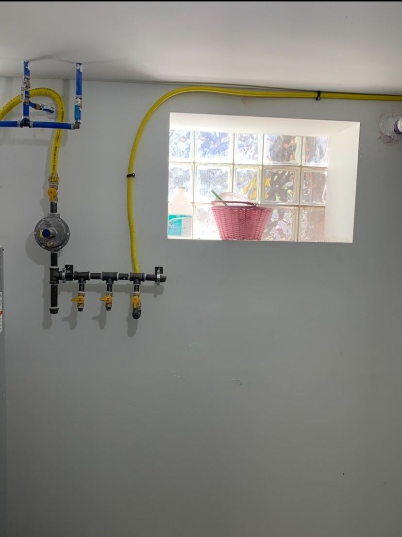 A gas manifold and pressure regulator with yellow corrugated piping mounted on a white wall near a glass block window.