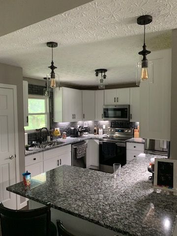 A modern kitchen featuring white cabinets, dark granite countertops, stainless steel appliances, and hanging light fixtures.