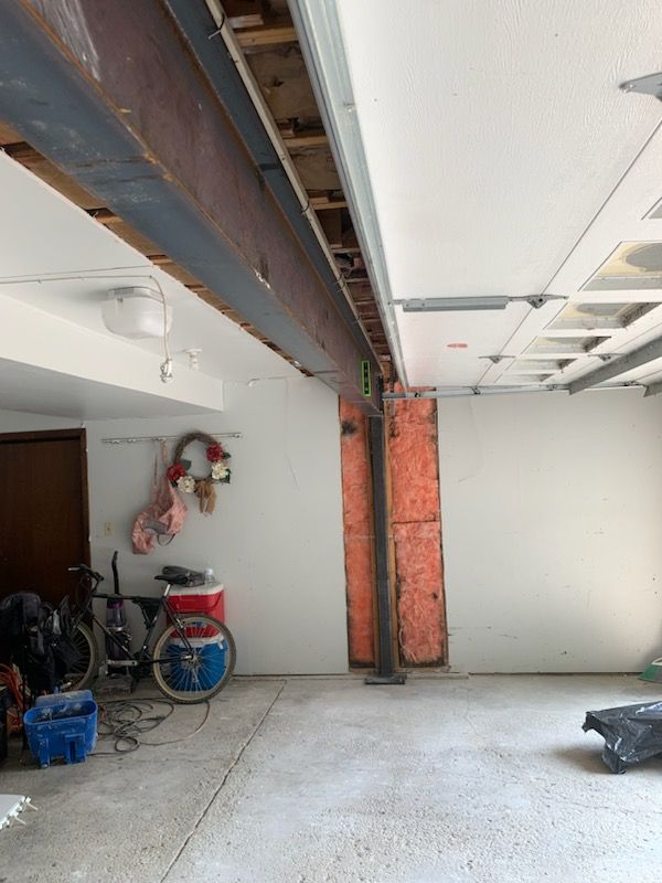 An unfinished garage interior showing a steel support beam, exposed wall insulation, and a bicycle near the back corner.
