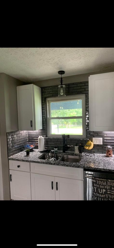 A kitchen sink area features white cabinets, granite countertops, and a dark mosaic tile backsplash under a window.