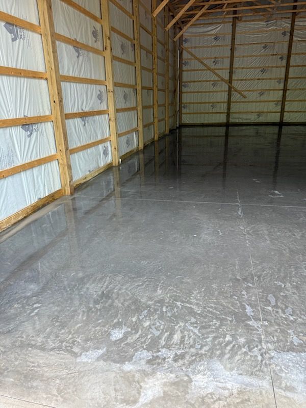Empty metal-framed warehouse with a wet concrete floor and white insulated walls