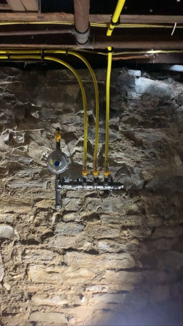 Yellow gas lines connected to a manifold mounted on a stone basement wall.