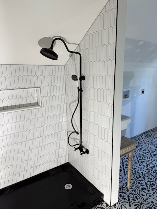 A shower with white pill-shaped wall tiles, a black floor tray, and a matte black rainfall showerhead and hand sprayer.