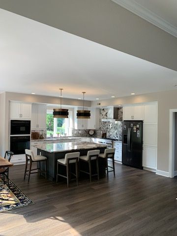 A modern kitchen with white cabinetry, a dark central island with four bar stools, and a black refrigerator.