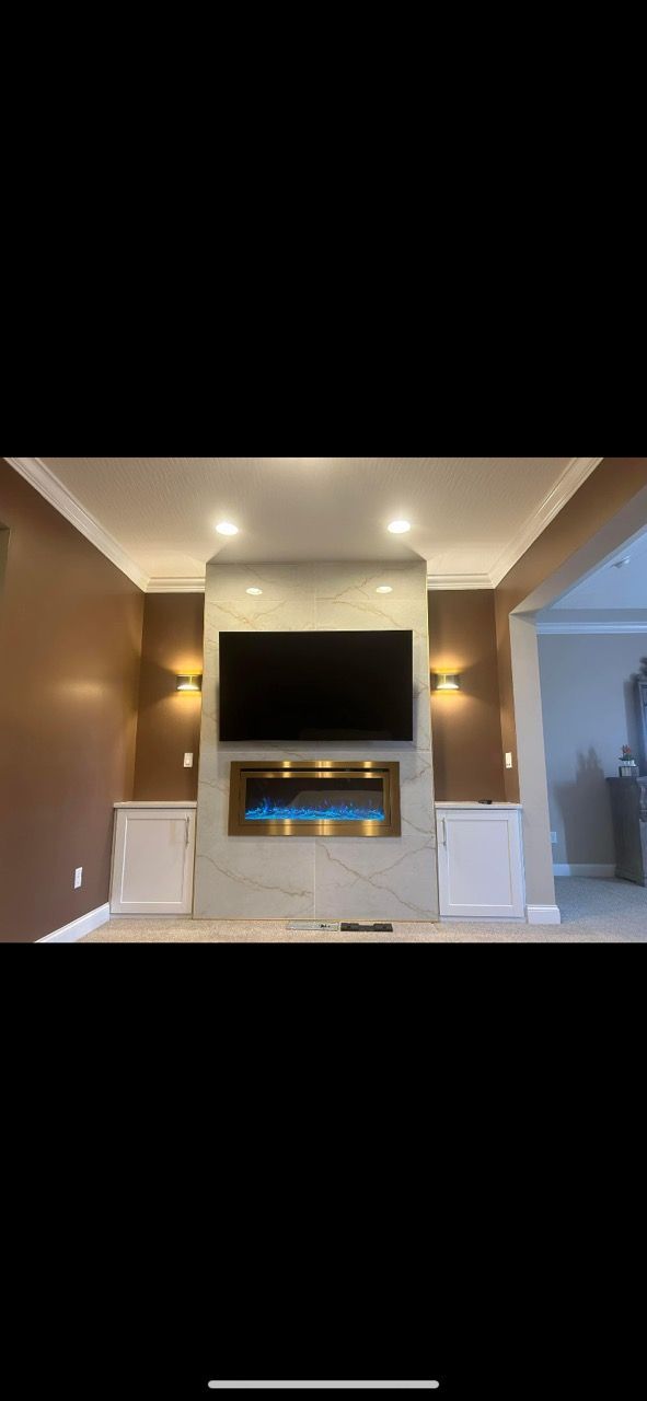 A wall-mounted TV sits above a glowing electric fireplace, flanked by wall sconces and built-in cabinets in a living room.