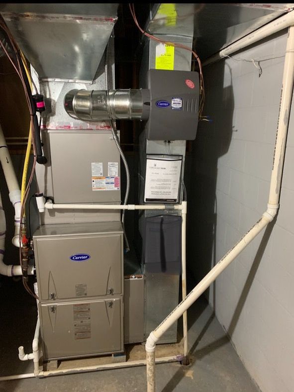 A Carrier HVAC furnace unit and ductwork system with an attached humidifier installed in a basement.