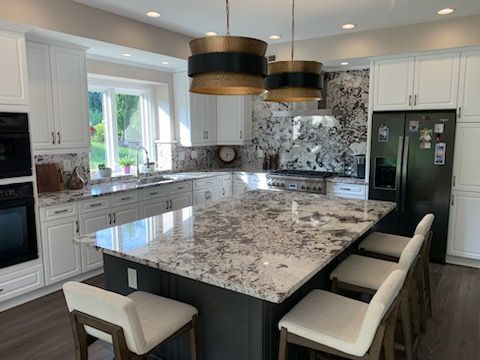 A kitchen with white cabinets, a dark gray island with granite countertops, bar stools, and two large pendant lights.