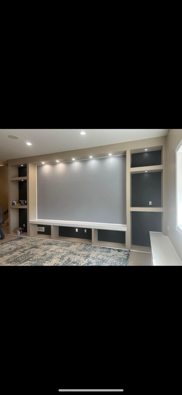A wall-mounted media unit with a large central screen, recessed lighting, and dark grey shelving in a contemporary room.