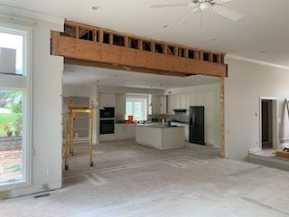 Renovated interior space showing a large, exposed wooden structural beam over a transition to a kitchen area.