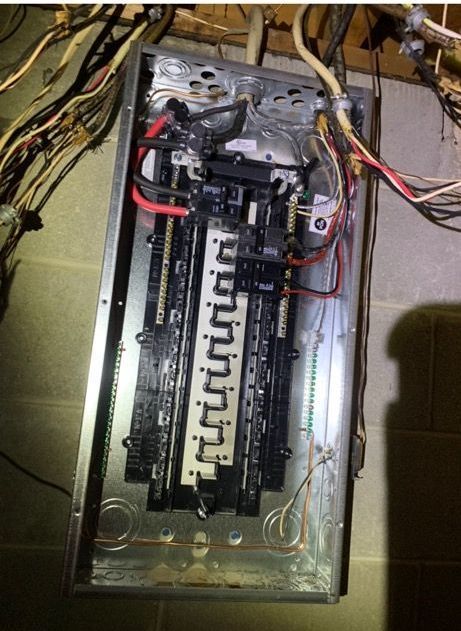 An open electrical breaker panel with red and black main power wires connected to a central terminal block.