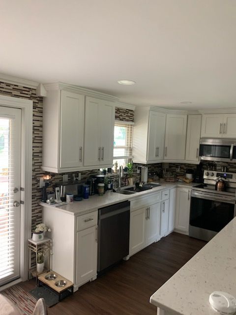 A bright kitchen with white cabinets, dark countertops, stainless steel appliances, and a tiled backsplash.