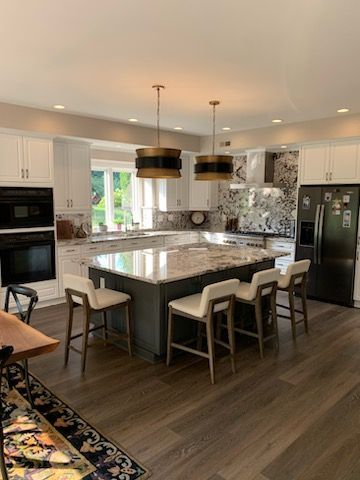 A bright modern kitchen with a dark gray central island, granite countertops, four white bar stools, and two pendant lights.