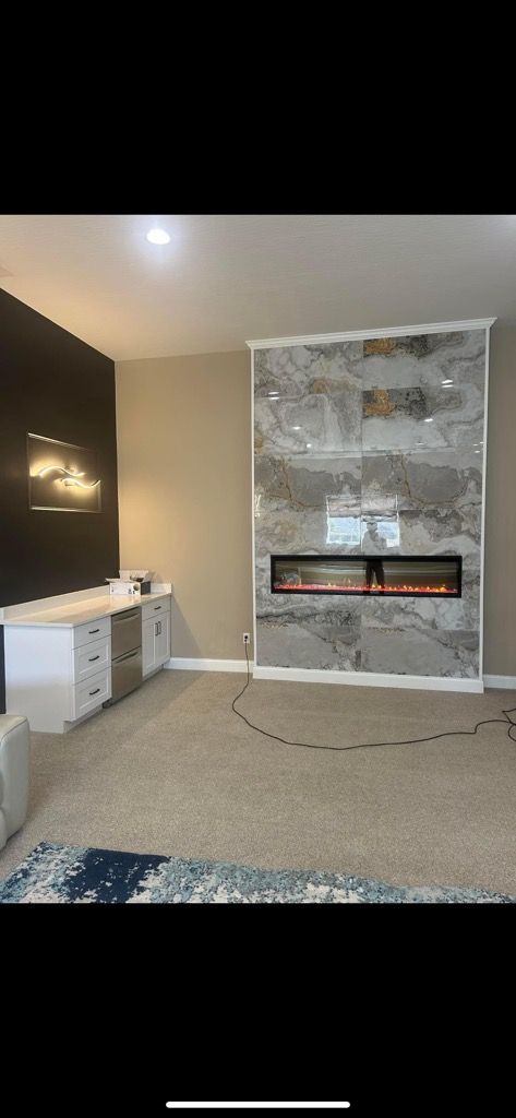 A living room features a tall fireplace with a gray marble tile surround and a black accent wall with white cabinets.