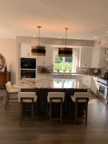 A kitchen with white cabinets, a large granite island, four modern bar stools, and two pendant lights above the island.