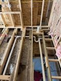 View from above showing white plumbing pipes installed between wooden floor joists in an unfinished room.