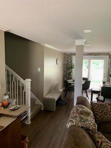 A staircase leads upward beside a neutral-toned wall with a bench, opening into a dining area with patterned wallpaper.