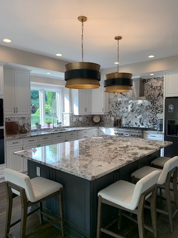 Modern kitchen with a dark gray island, light granite countertops, white cabinets, and two bronze and black pendant lights.
