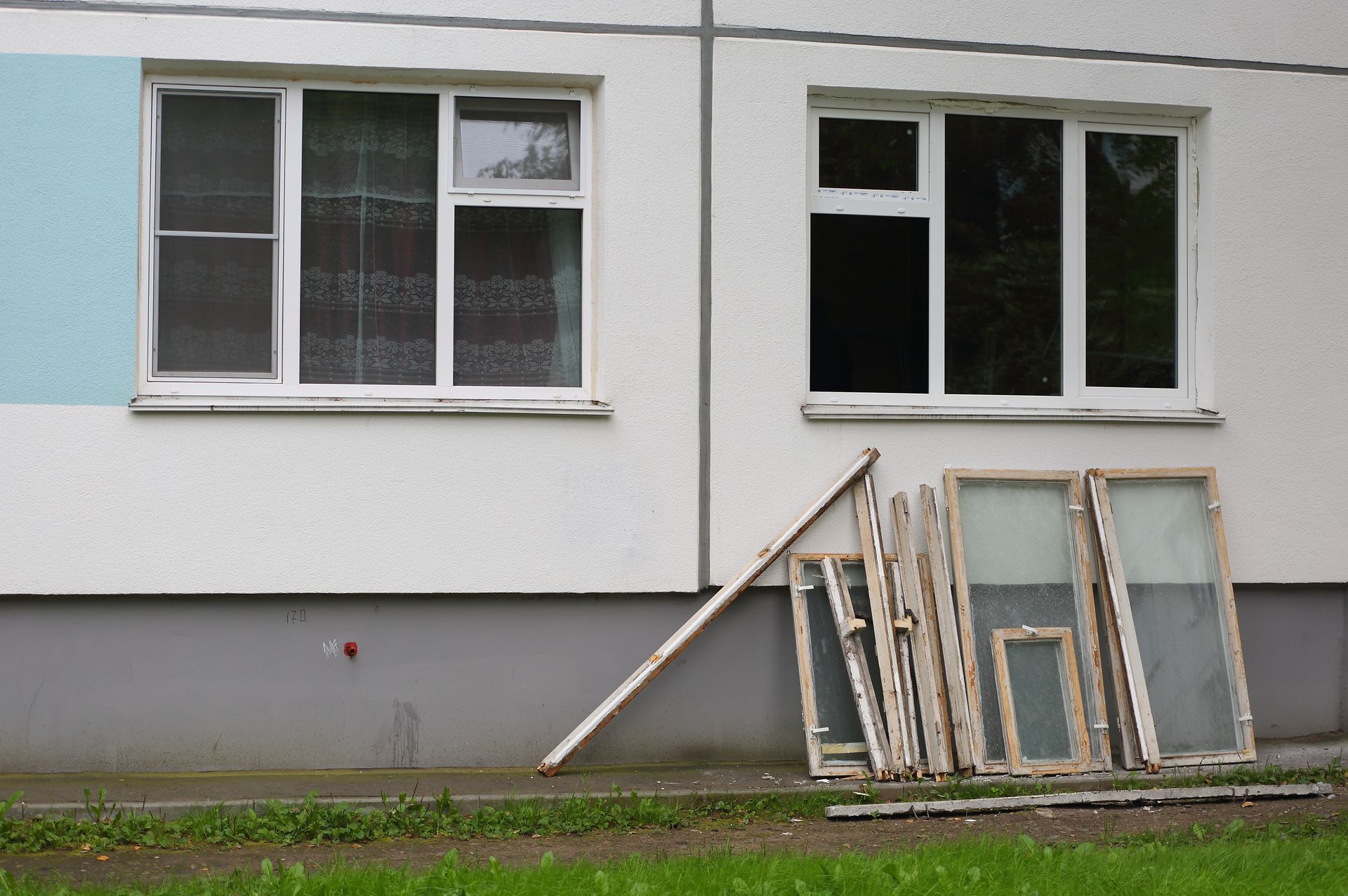 Old window frames leaned against the white wall of a building below two installed windows.