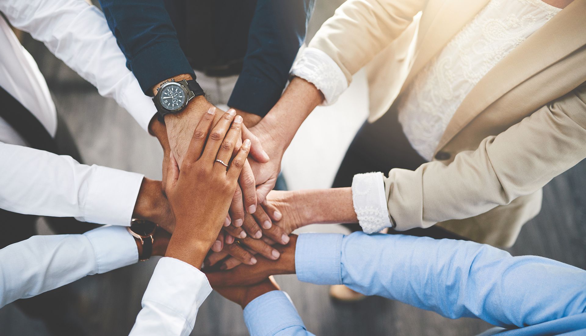 Hands of diverse people stacked in a team huddle, symbolizing unity.