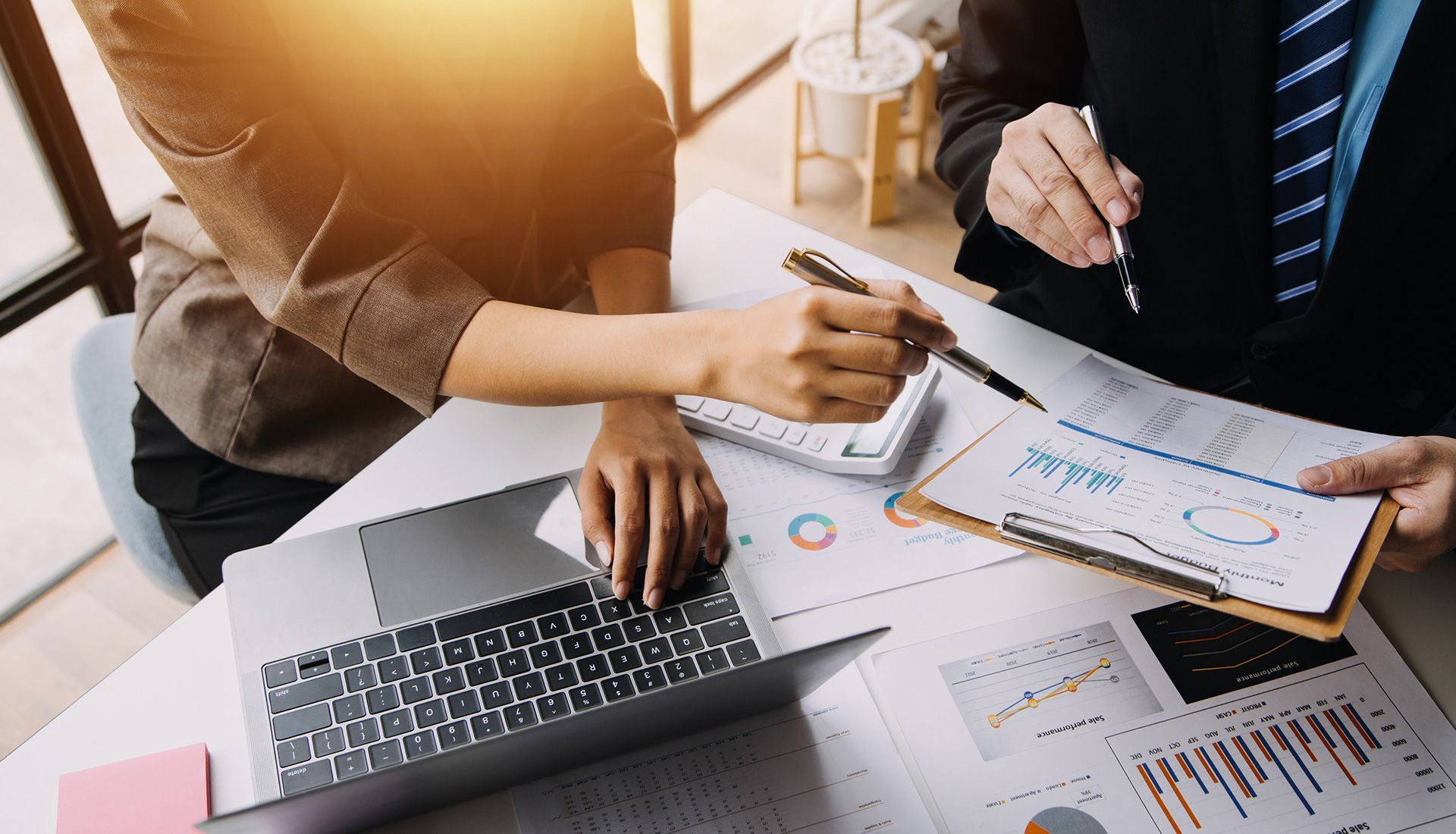 Two people analyzing financial data on a laptop and documents at a desk.