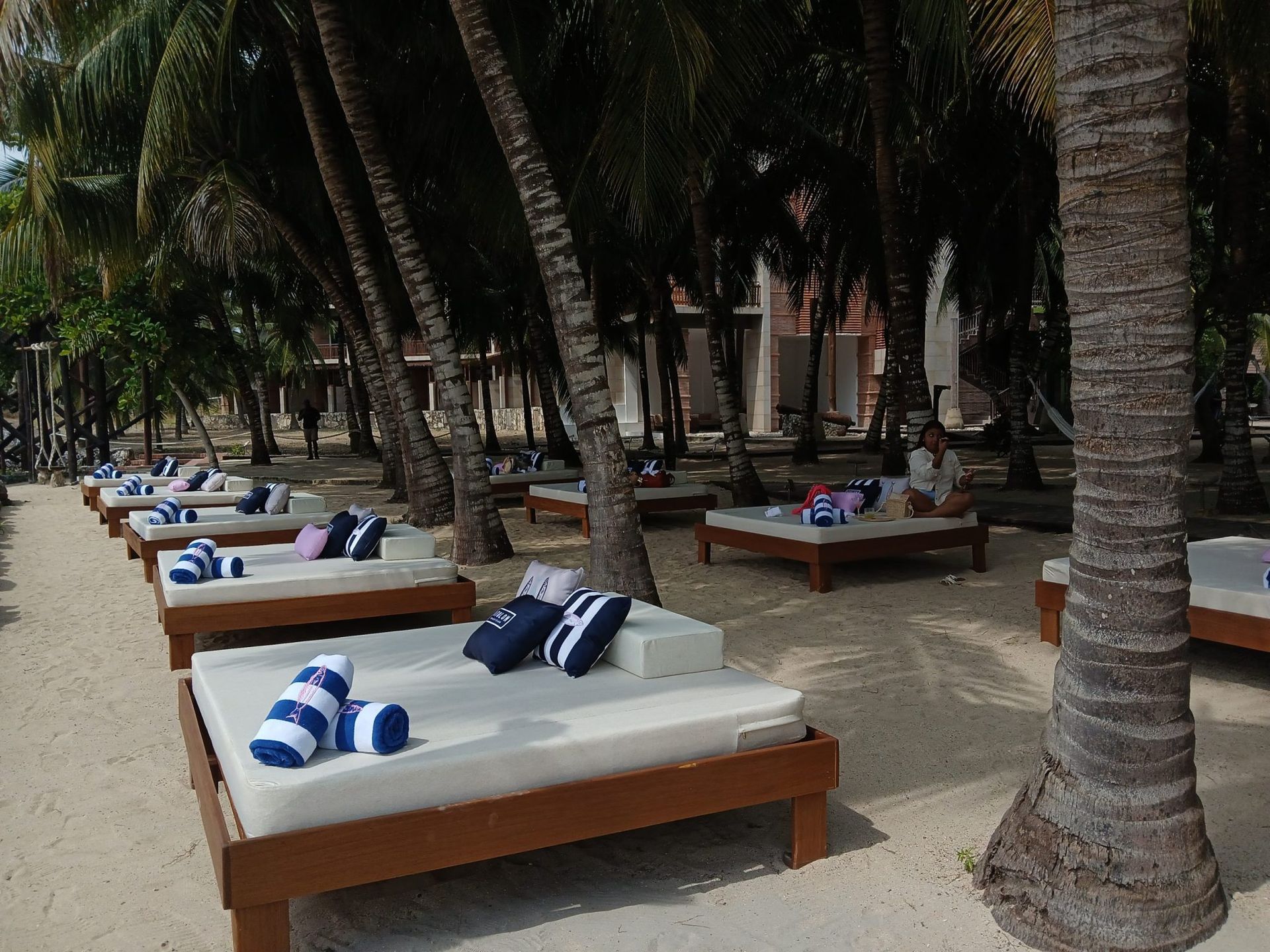 Tumbonas bajo palmeras. Cojines blancos, toallas a rayas azules y almohadas sobre la arena de la playa.
