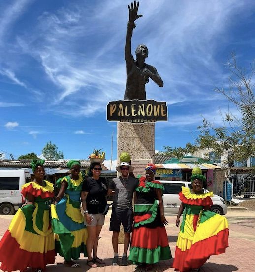 Grupo posando frente a una estatua en Palenque, Colombia; personas vestidas con coloridos trajes tradicionales.