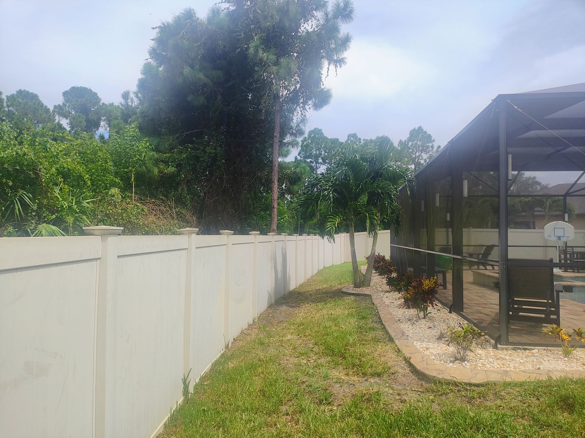 A white fence surrounds a lush green yard next to a house.