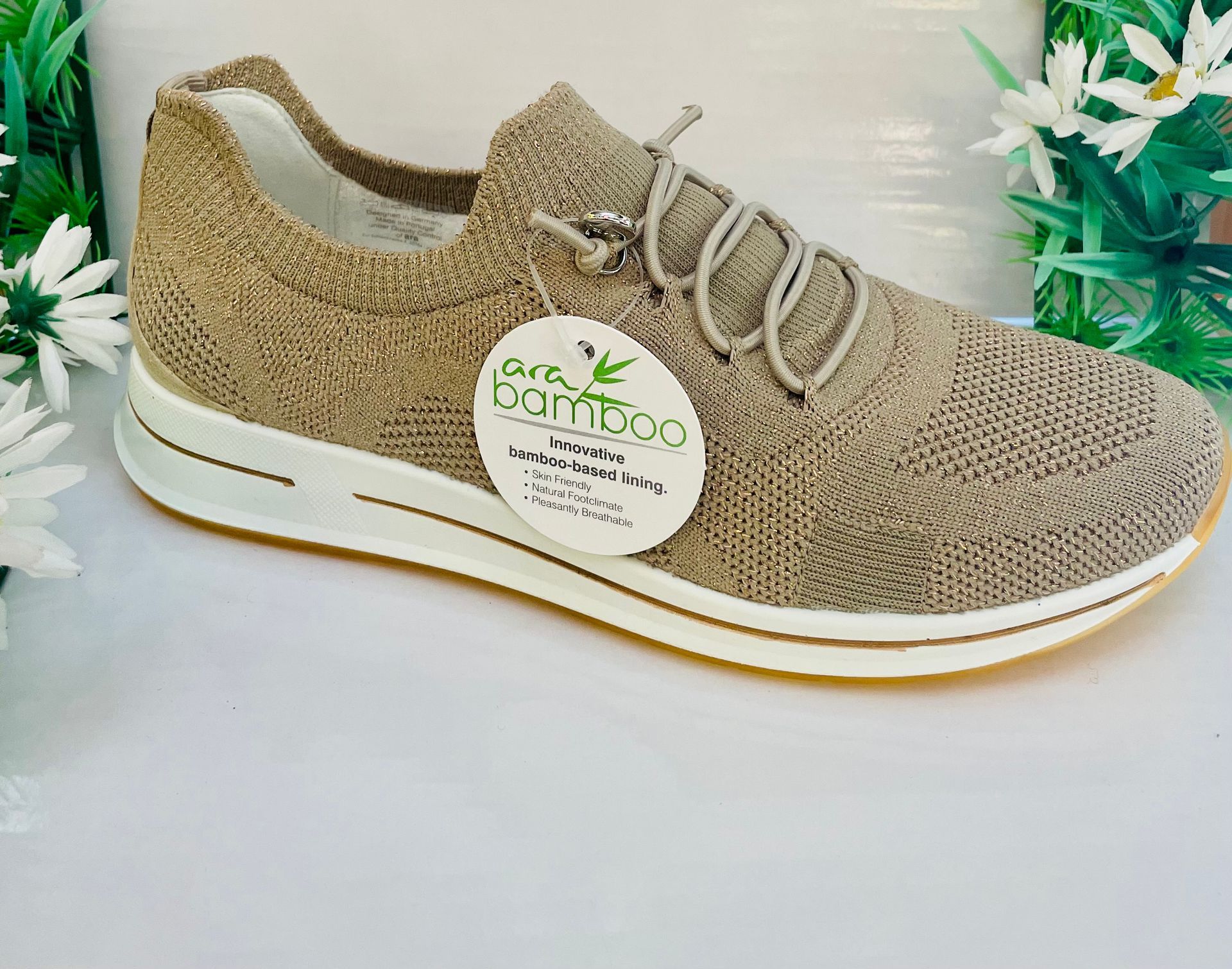 Scarpa in maglia color cuoio con suola bianca, etichetta in bambù e lacci decorativi.