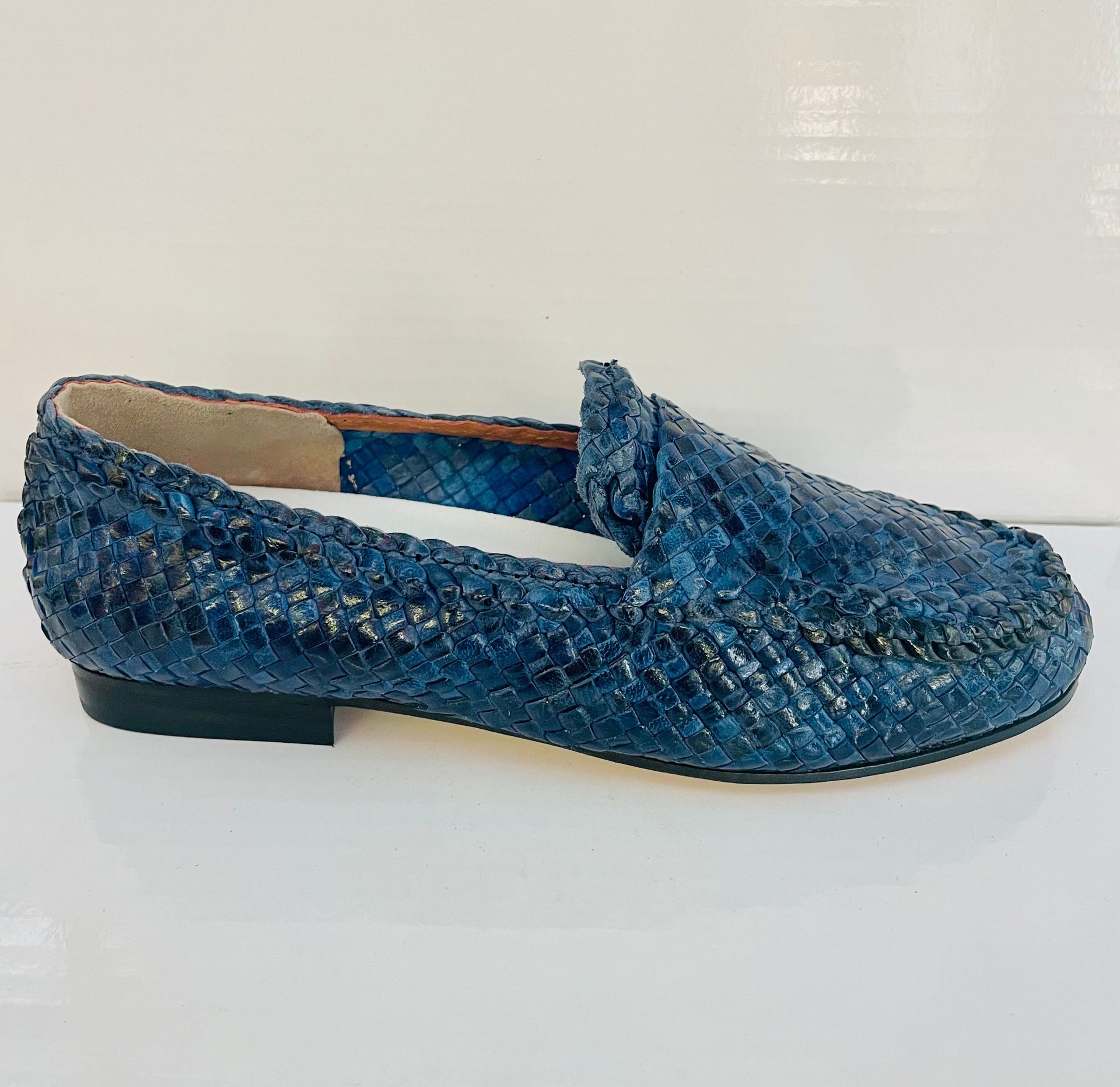 Mocassino in pelle intrecciata blu su una superficie bianca.