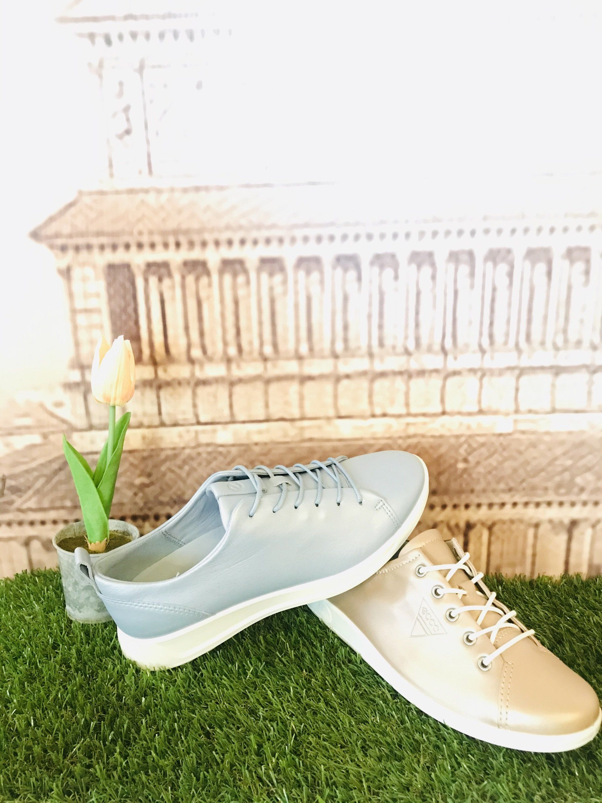 Due paia di scarpe da ginnastica sull'erba verde. Una è azzurra e l'altra beige, entrambe con suola e lacci bianchi.
