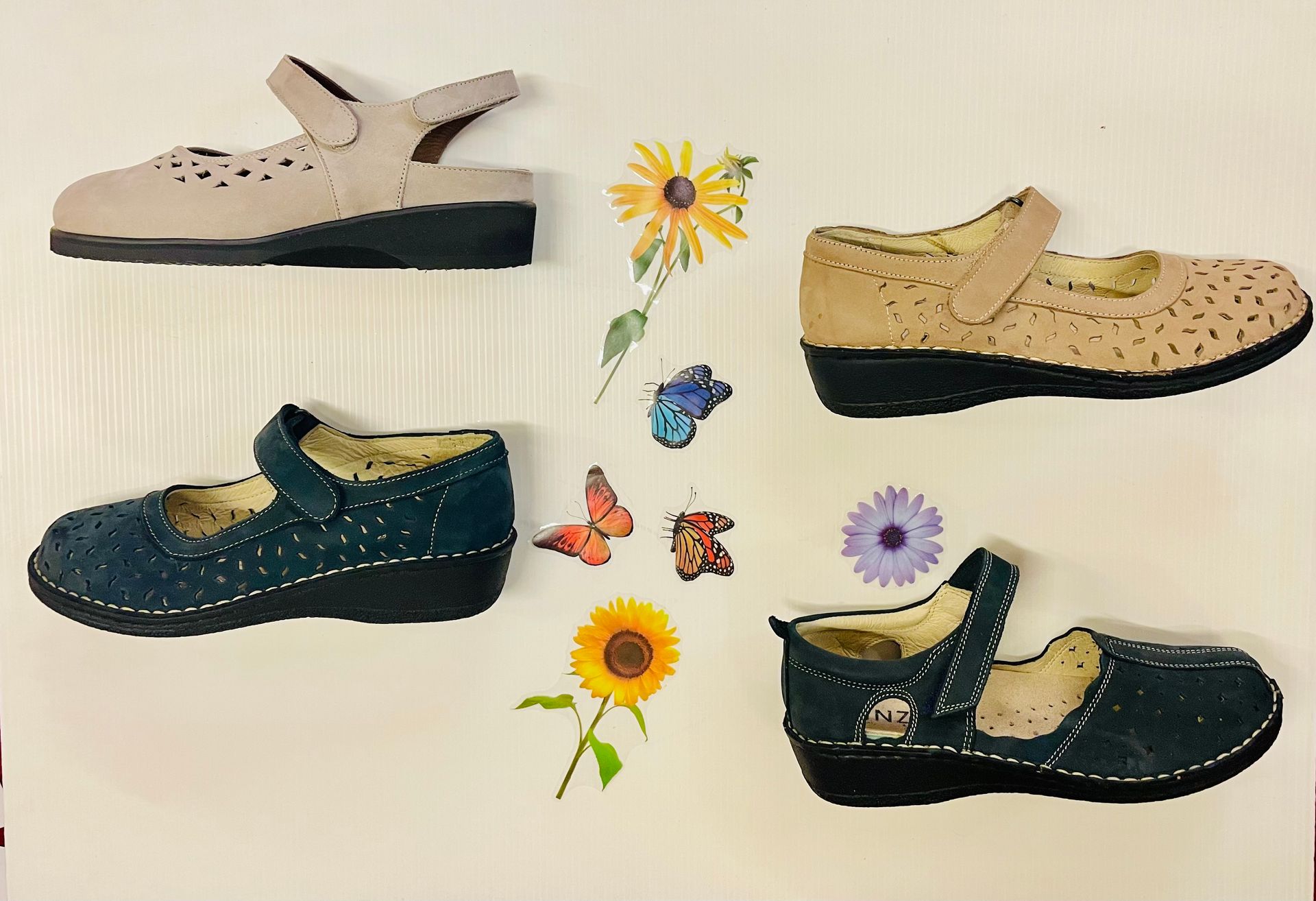 Quattro paia di scarpe in pelle in stile Mary Jane: beige, marrone chiaro e blu scuro con suole nere, più adesivi con fiori e farfalle.