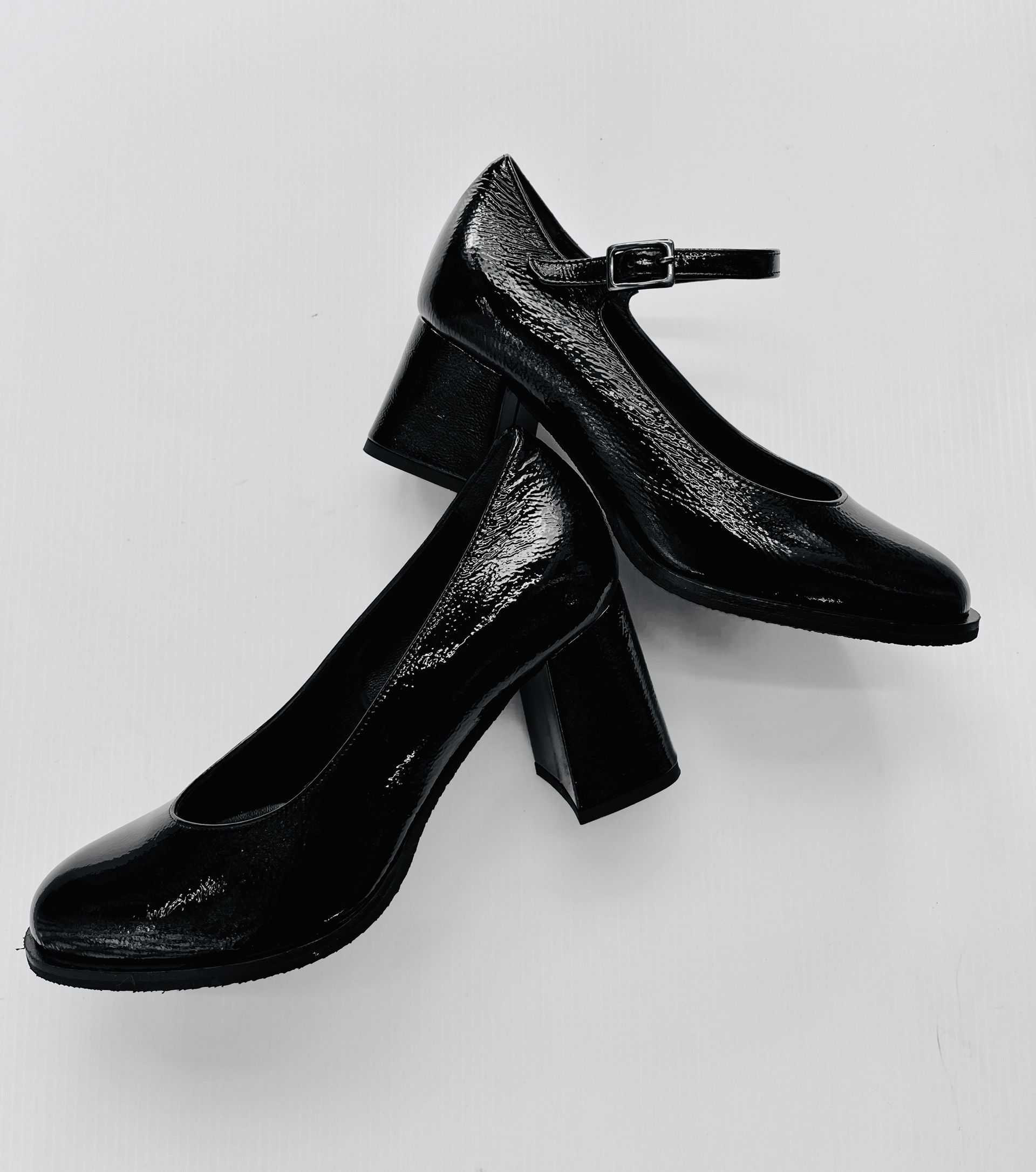 Scarpe Mary Jane con tacco in vernice nera su superficie bianca.
