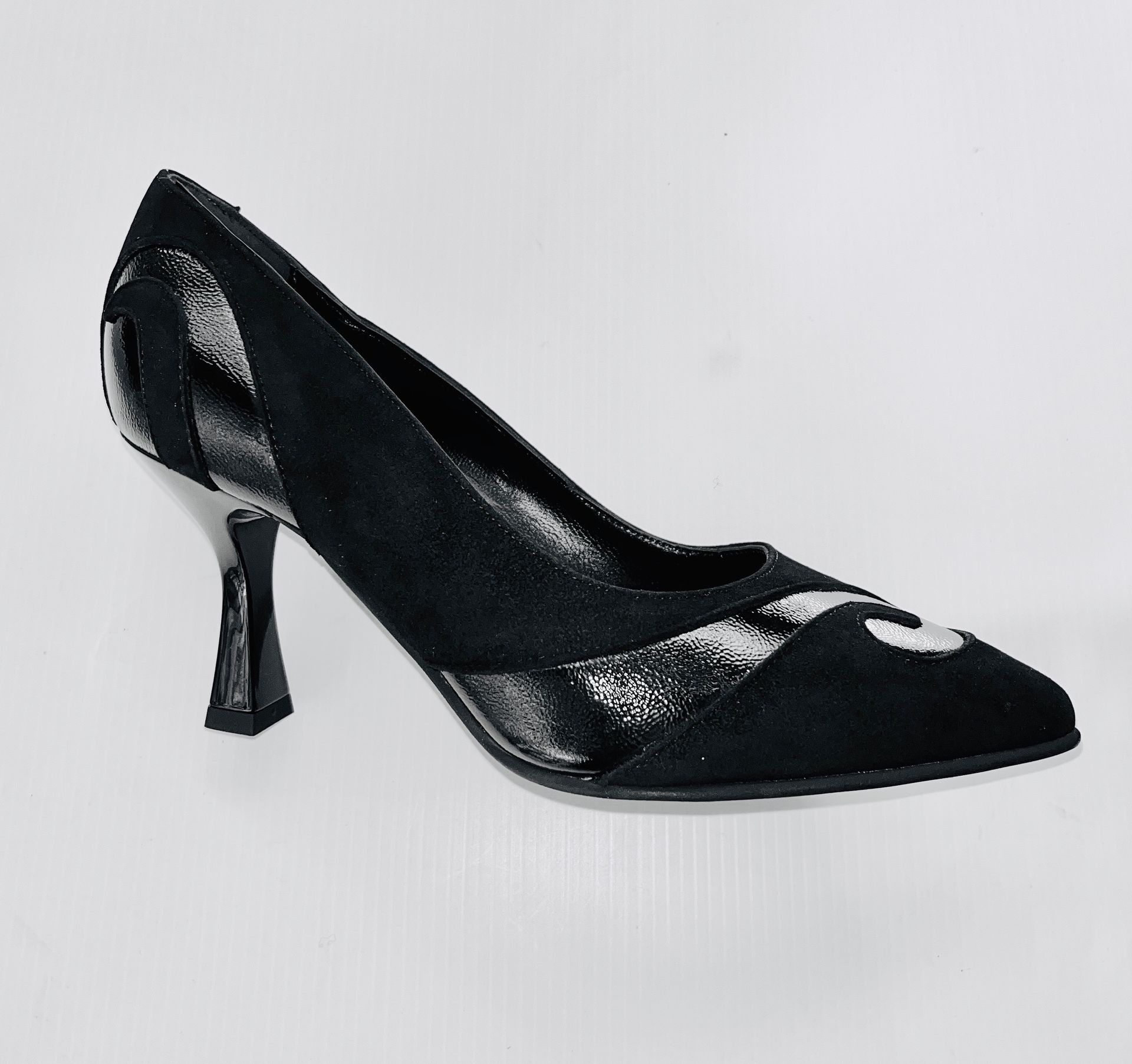 Scarpa nera con tacco alto, punta affilata e motivo decorativo su sfondo grigio.
