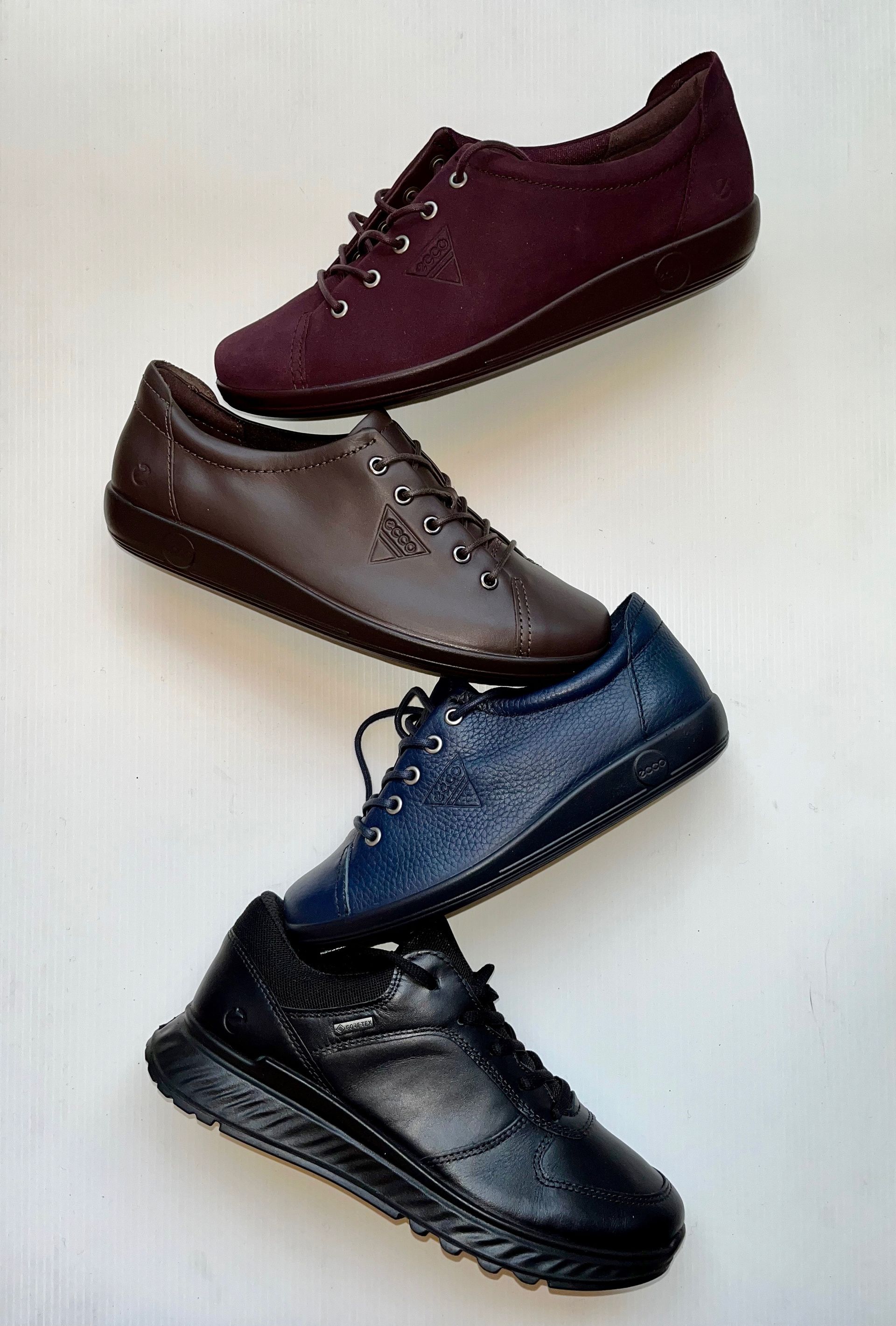 Quattro paia di scarpe da ginnastica in pelle color bordeaux, marrone, blu e nero, disposte leggermente obliquamente.