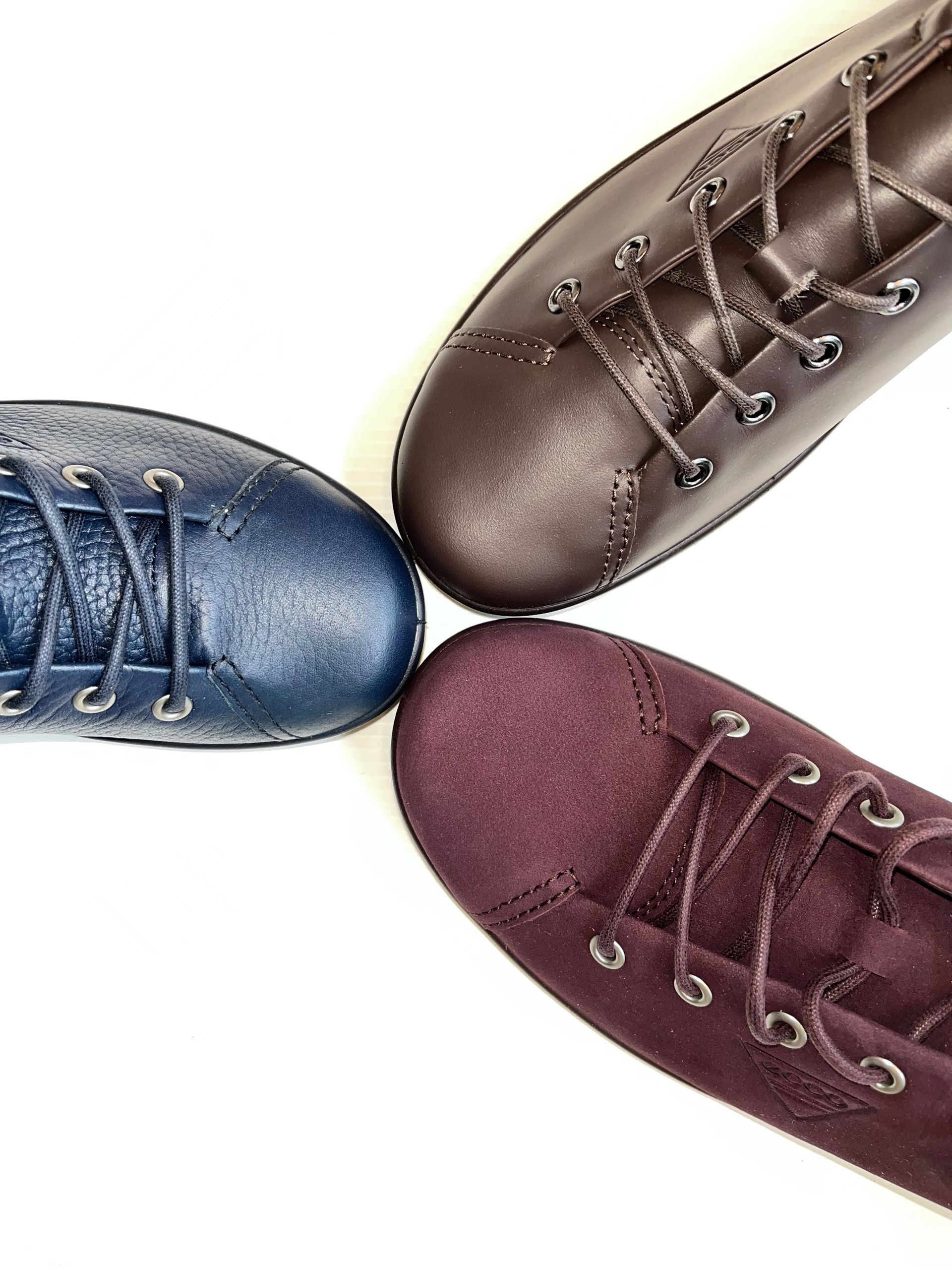 Quattro scarpe di pelle blu, marrone e viola disposte in cerchio.