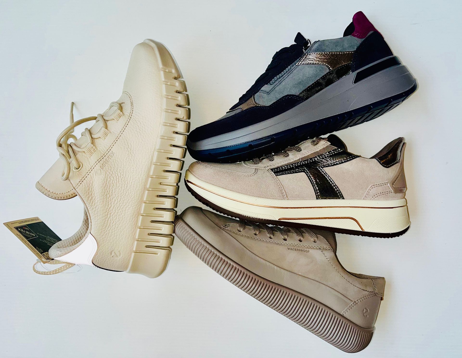 Quattro paia di scarpe da ginnastica da donna di diversi colori e stili, disposte su una superficie bianca.