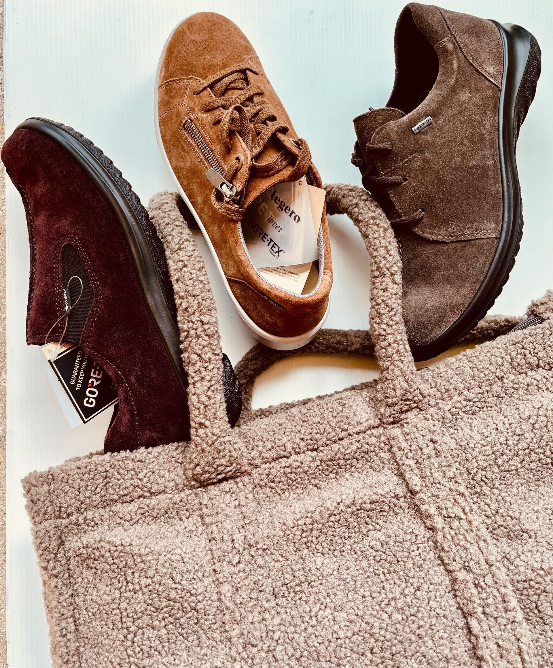 Tre paia di scarpe marroni in una borsa di tela color cuoio su una superficie bianca.