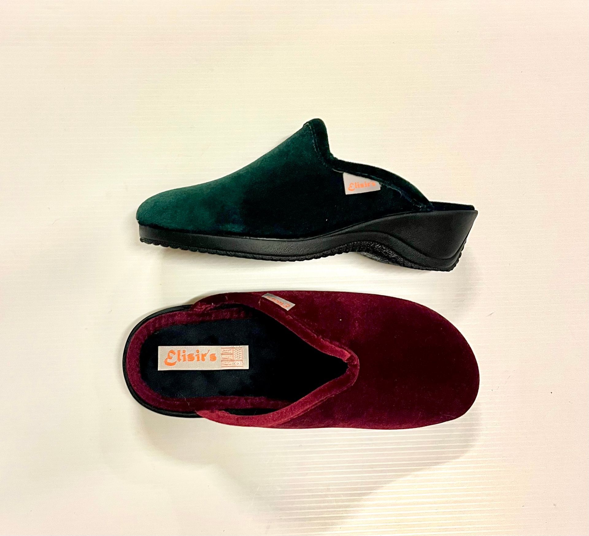 Due pantofole di velluto: una verde smeraldo, una bordeaux, su una superficie color crema.