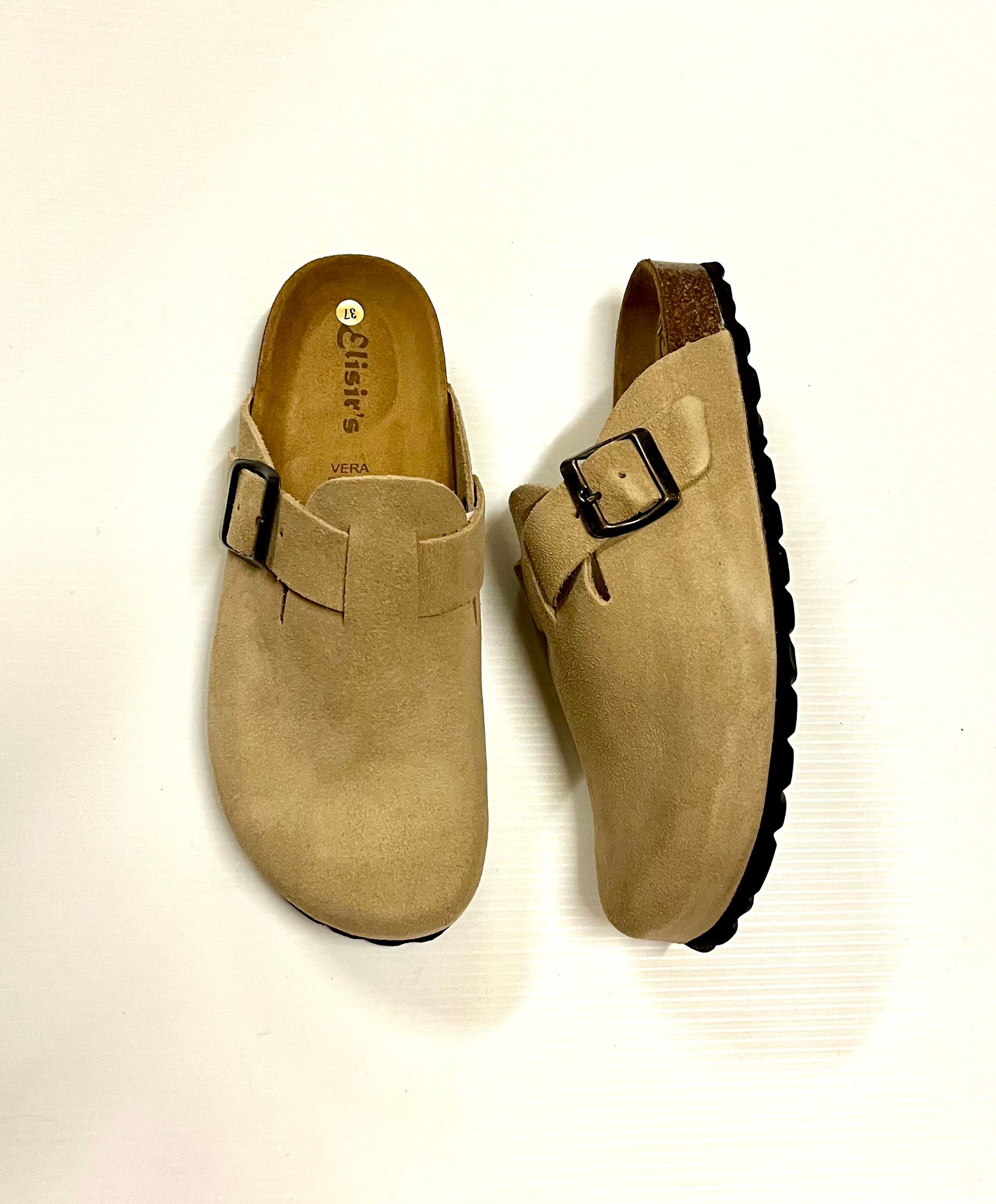 Due zoccoli in pelle scamosciata beige con fibbie nere su sfondo bianco.