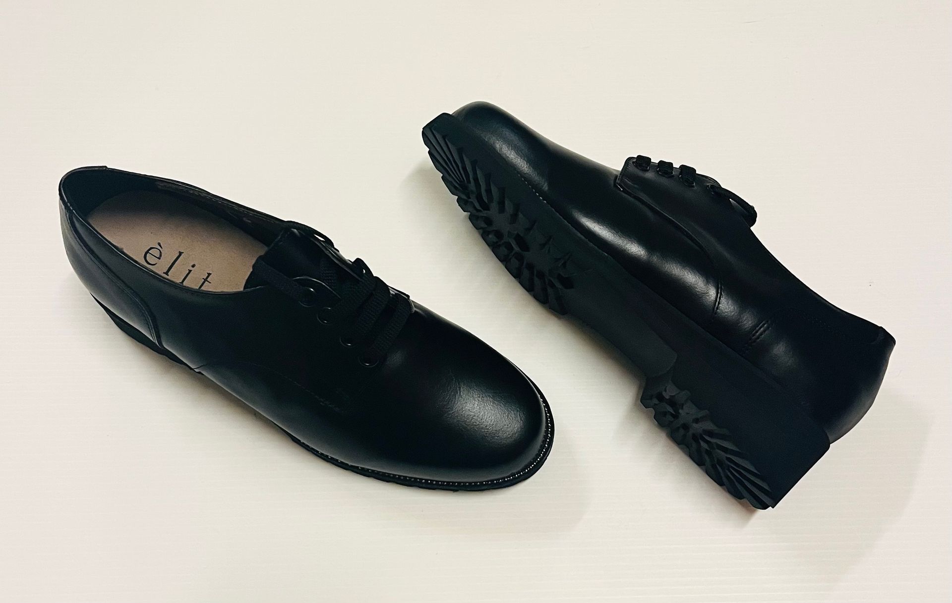 Un paio di scarpe di pelle nera su una superficie bianca, una scarpa in verticale e l'altra di lato.
