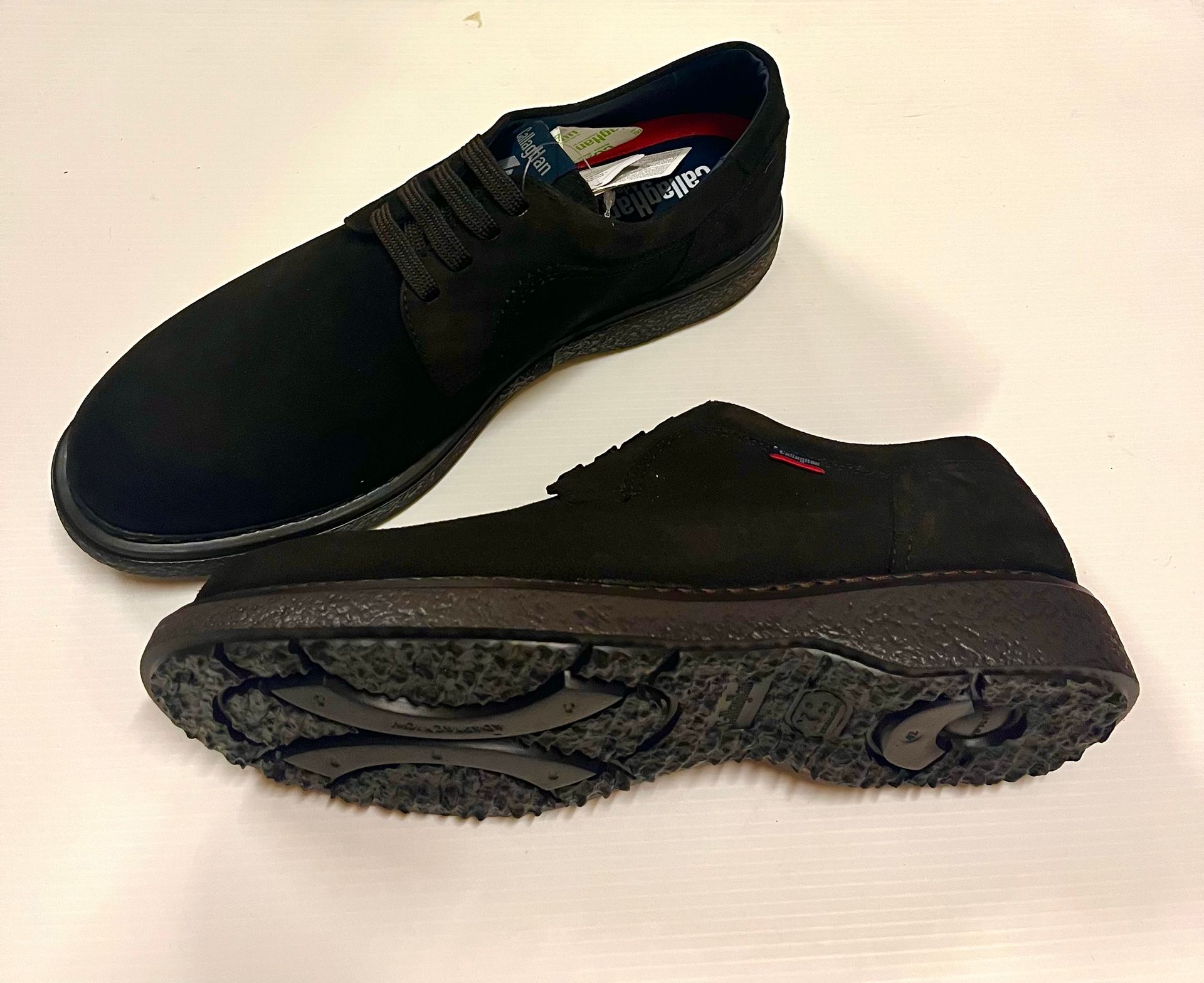 Due scarpe slip-on in pelle scamosciata nera su una superficie bianca, una in verticale e l'altra di lato, con la suola visibile.