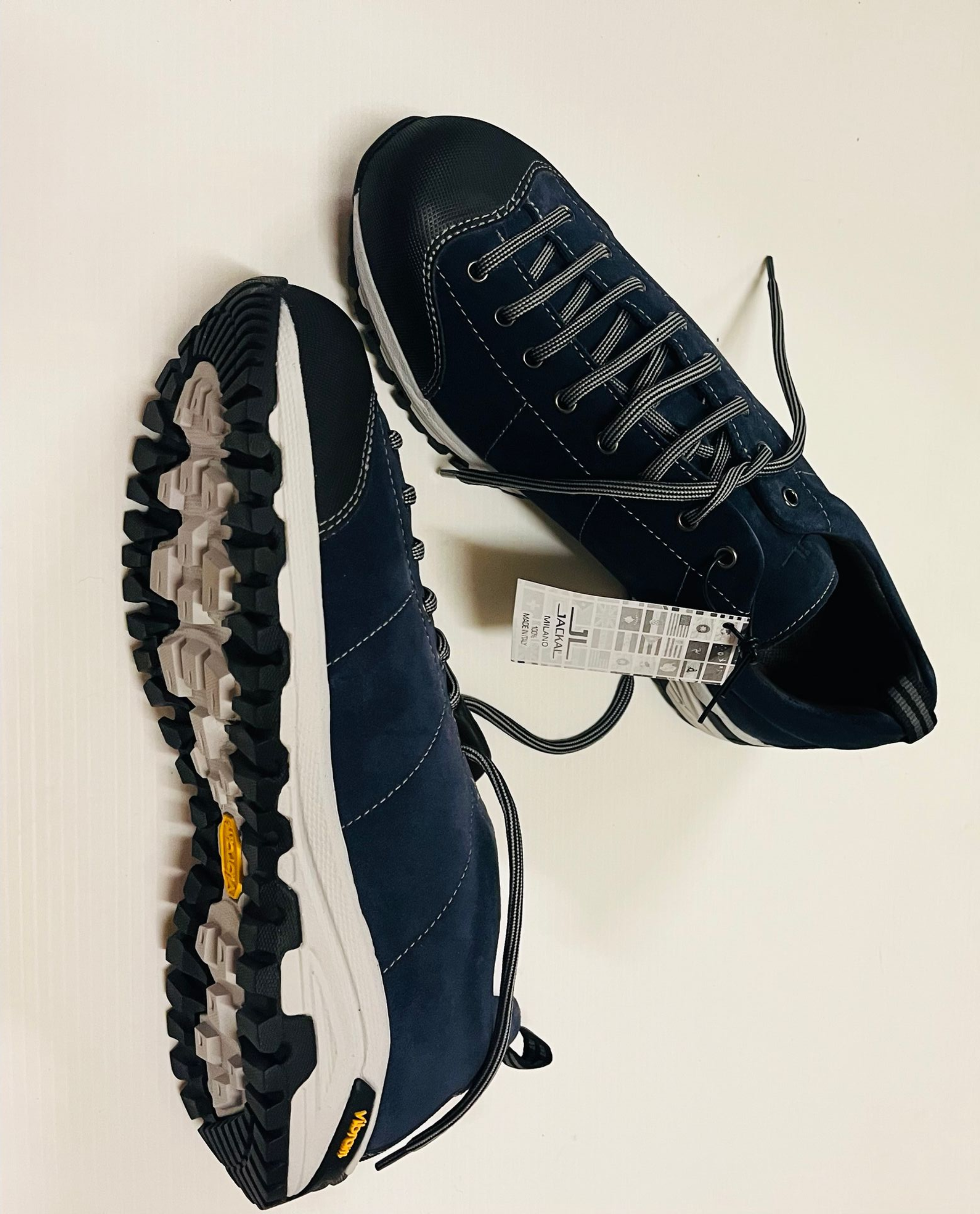 Scarpe da trekking blu navy con suola bianca, battistrada Vibram e etichetta su superficie bianca.