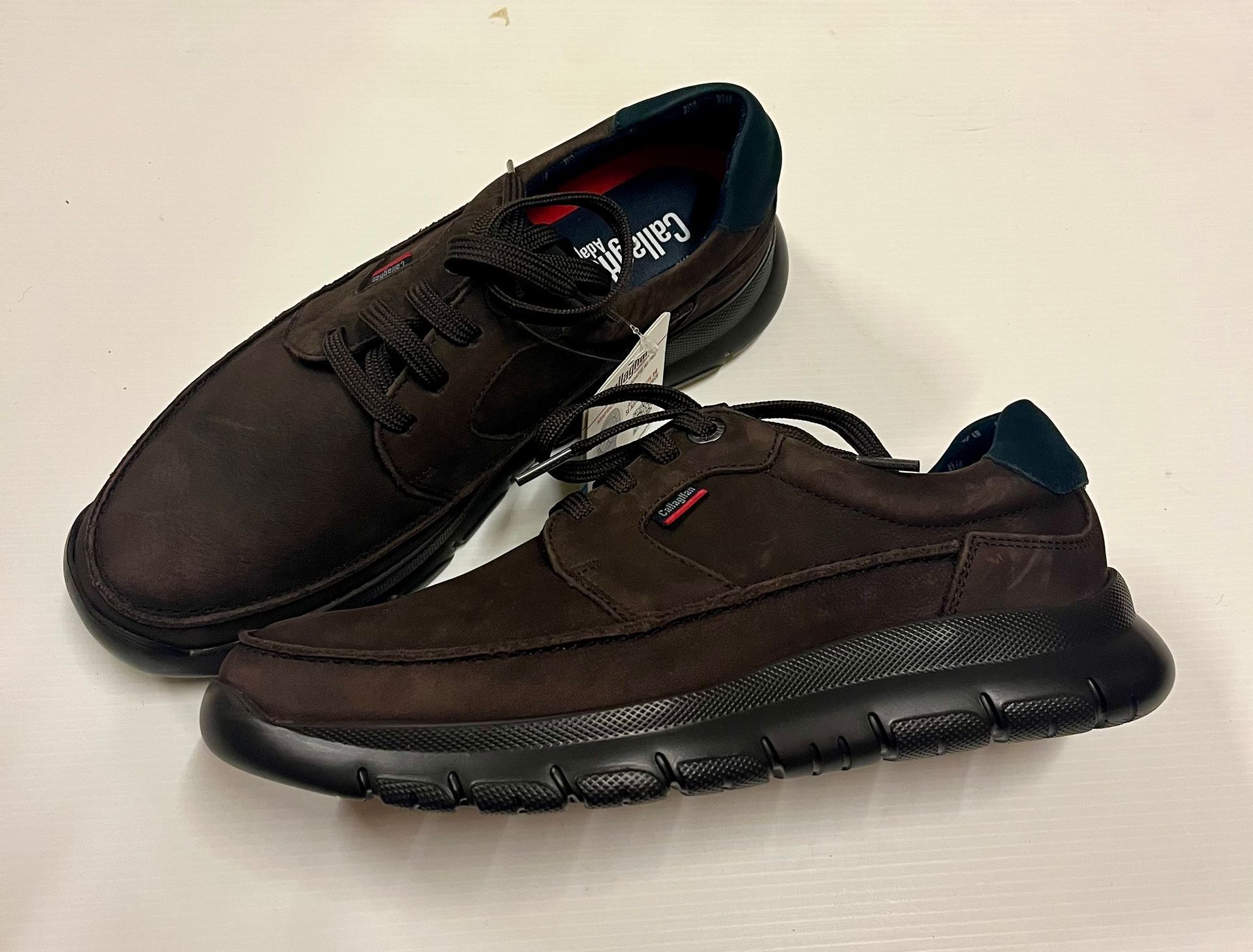Due scarpe scamosciate marroni con suola e lacci neri su una superficie bianca.