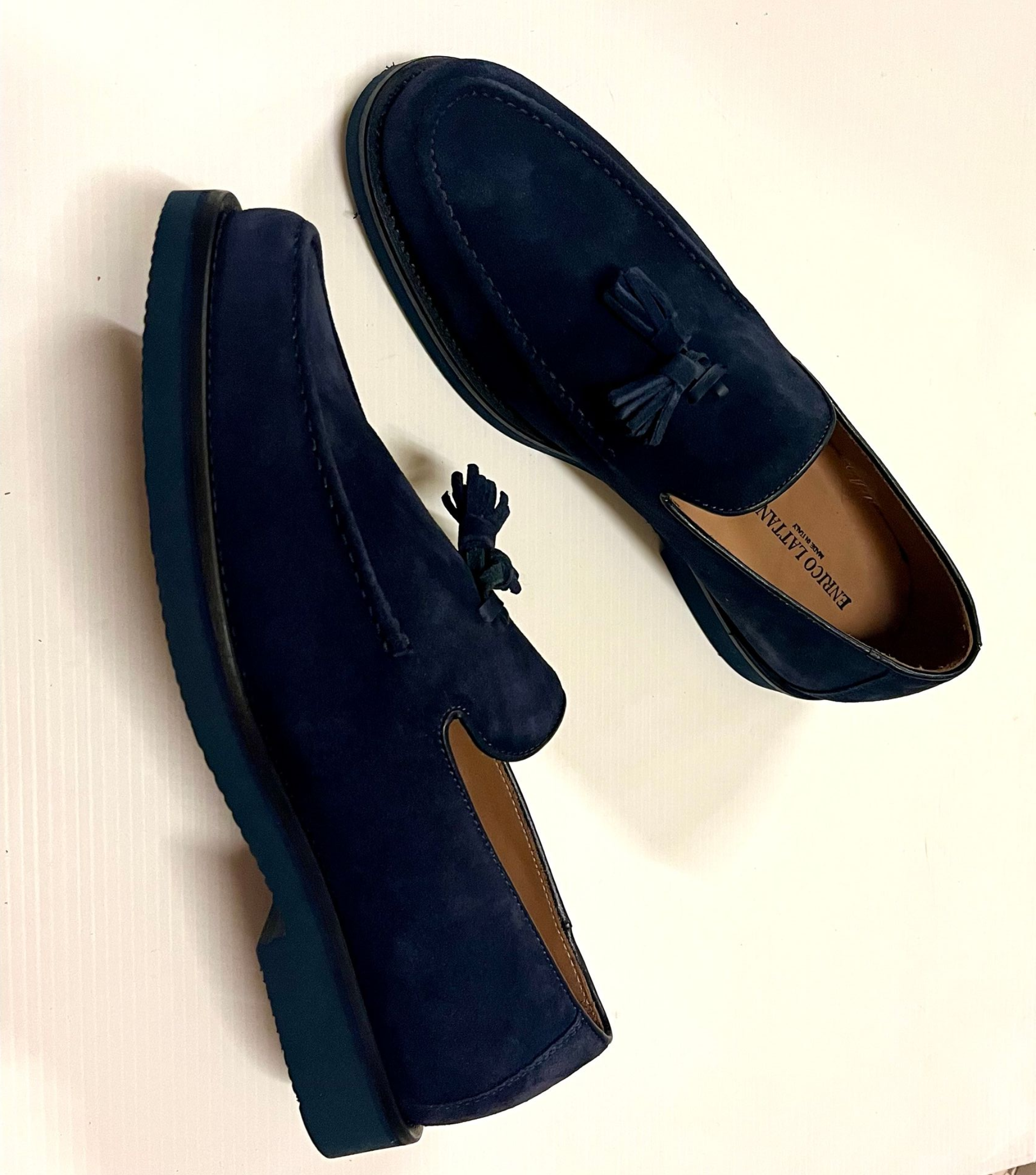 Un paio di mocassini con nappe in pelle scamosciata blu navy su una superficie bianca.
